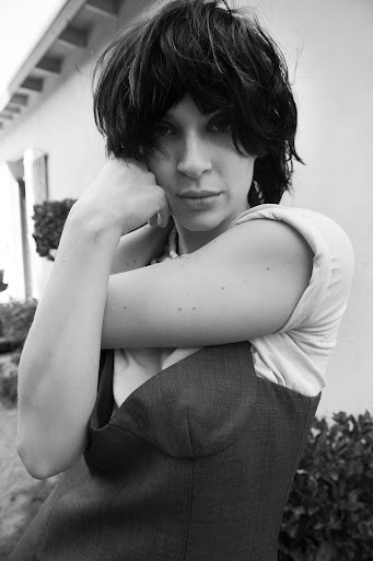 Black and white portrait of an adult woman with dark, short hair, wearing a dark vest with a white shirt. She is resting her face on her hand.