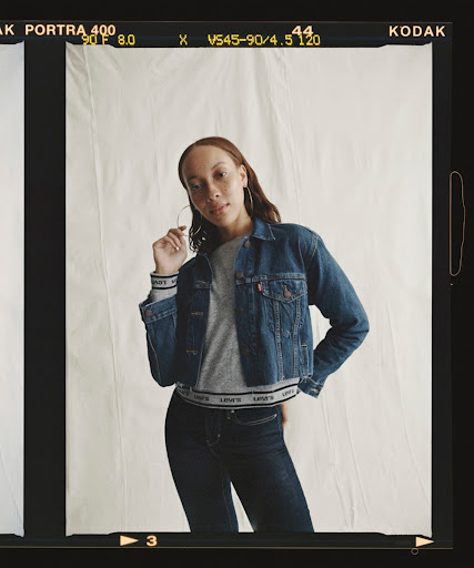 Woman poses in a denim jacket and dark jeans against a neutral backdrop, framed by Kodak film borders in a medium indoor shot.