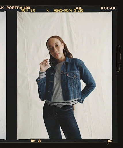 Woman poses in a denim jacket and dark jeans against a neutral backdrop, framed by Kodak film borders in a medium indoor shot.