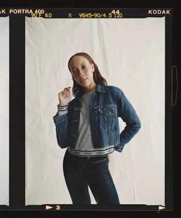 Woman poses in a denim jacket and dark jeans against a neutral backdrop, framed by Kodak film borders in a medium indoor shot.