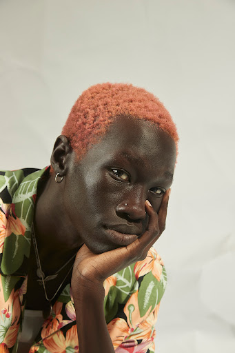 Portrait of an adult male with light pink hair wearing a floral-patterned shirt, looking at the camera in an indoor setting.