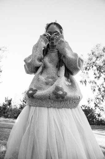 Black and white low angle shot of a smiling young woman wearing a floral sweater and tulle skirt making a heart shape with her hands.