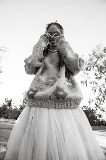 Black and white low angle shot of a smiling young woman wearing a floral sweater and tulle skirt making a heart shape with her hands.