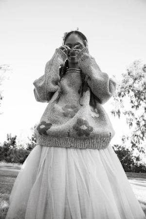 Black and white low angle shot of a smiling young woman wearing a floral sweater and tulle skirt making a heart shape with her hands.