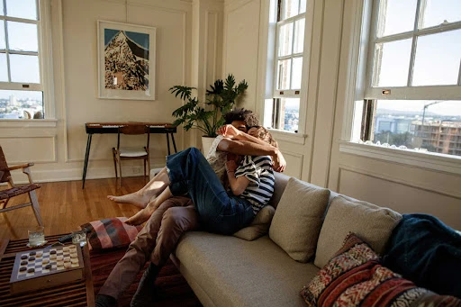 A man and a woman embracing on a living room sofa styled by fashion stylist Gena Tuso.