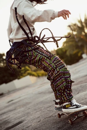 Low angle shot of a person skateboarding outdoors wearing a light grey hoodie and patterned textured trousers styled by Gena Tuso.