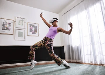 Person wearing VR headset and purple tank top striking a dynamic dance pose in a bright living room
