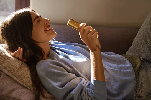 Adult woman lying on a couch, holding a gold object, smiling with natural lighting and a casual aesthetic. Relaxed indoor setting.