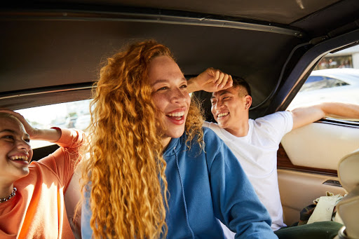Three friends ride in the back of a vintage convertible with the top down, laughing in the sunshine. Lifestyle, friendship concept.