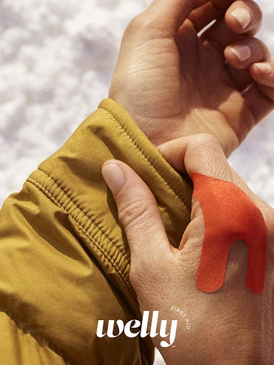 Close-up of a person's hand with an orange bandage on their skin against a background of snow and wearing a yellow jacket.