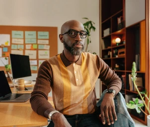 Black man wearing striped brown polo shirt and glasses seated in a home office