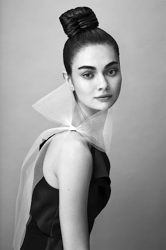 Black and white portrait of a stylish woman with a high bun, wearing a black dress and a white tulle collar.