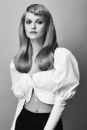 Black and white portrait of a woman with long braided hair wearing a white puff-sleeve top against a grey seamless background