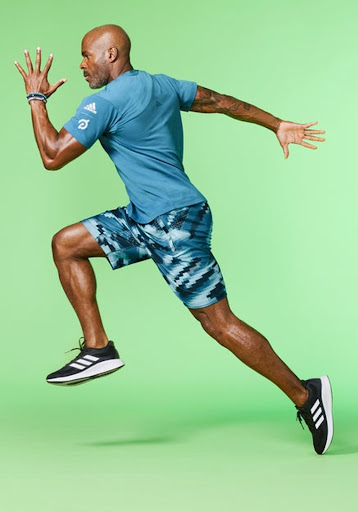 Athletic Black man in sportswear mid-stride in a full shot against a bright green backdrop, showcasing fitness and motion.