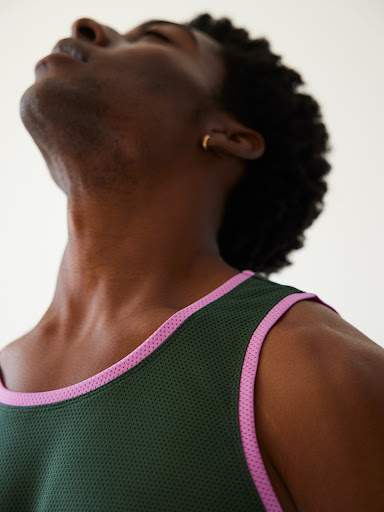 Close-up studio shot of an African-American male model looking upwards, wearing a green tank top with light pink trim, against a plain white backdrop.