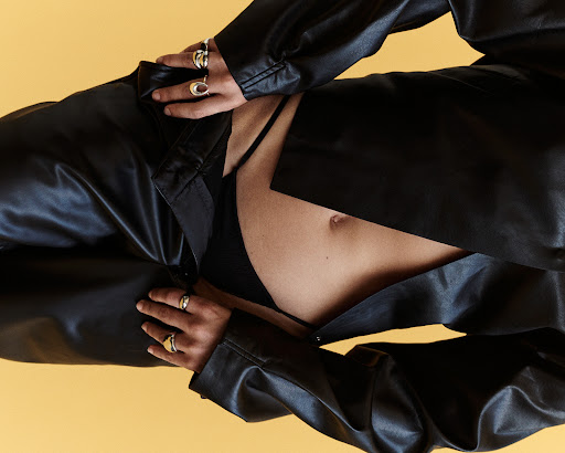 Close-up portrait of a model wearing a black leather shirt and trousers with silver rings against a warm yellow background