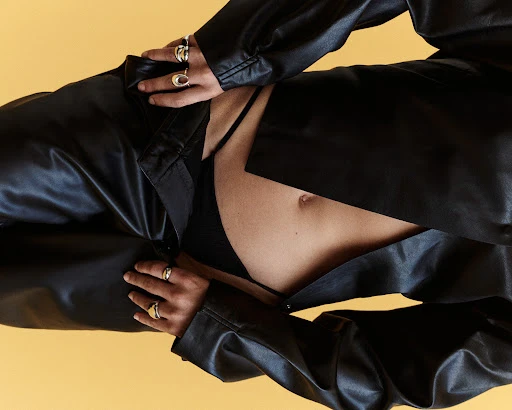 Close-up portrait of a model wearing a black leather shirt and trousers with silver rings against a warm yellow background