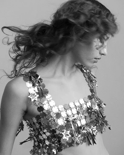 Black and white portrait of a woman wearing a shimmering metallic top. Head and shoulders shot with blurred hair and neutral background.