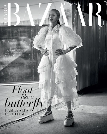 Black and white fashion editorial shot of Ramla Ali on Harper's Bazaar Arabia cover in a white tiered dress with puff sleeves and platform shoes.