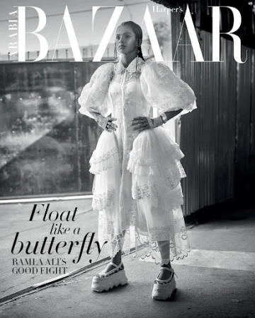 Black and white fashion editorial shot of Ramla Ali on Harper's Bazaar Arabia cover in a white tiered dress with puff sleeves and platform shoes.