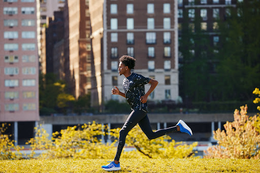 Athletic African American man running in a park with modern buildings in the background, wearing leggings and a printed shirt.