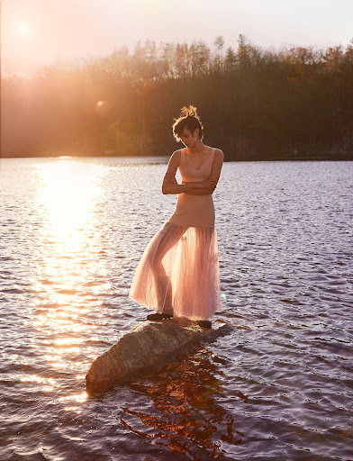 A person in a sheer pink dress standing on a rock in a lake during sunset, styled by Jèss Monterde.