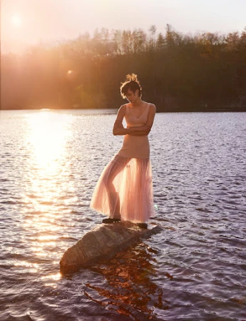 A person in a sheer pink dress standing on a rock in a lake during sunset, styled by Jèss Monterde.