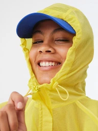 Smiling woman in a yellow hooded jacket and blue cap against a plain white background