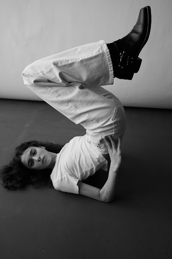 Monochrome portrait of a person lying on their back with legs raised in the air wearing denim jeans and black leather boots.