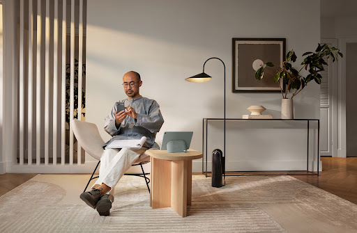Adult male using smartphone while sitting in a chair in a modern living room with natural light and minimalist decor.