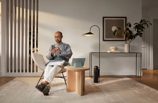 Adult male using smartphone while sitting in a chair in a modern living room with natural light and minimalist decor.