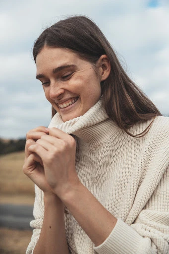 Portrait of an adult female fashion model with medium brown hair wearing a dark turtleneck sweater in a photo studio setting.