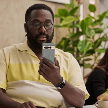 Black man wearing glasses and yellow striped shirt looking at a smartphone, styled by Lauren Knudsen.