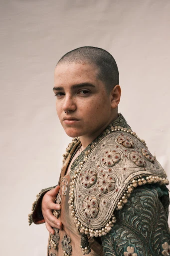 Portrait of a young person wearing a bullfighting costume, featuring ornate embroidery and embellishments, posing against a neutral background.