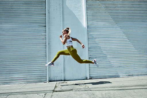 Athletic woman in workout clothes leaping in the air against a textured roll-up door. Active lifestyle, fitness, and urban environment.