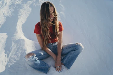 Woman with long hair wearing a red t-shirt and ripped blue jeans sitting on white sand dunes