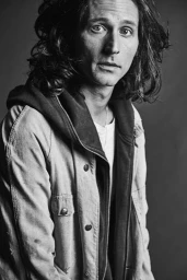 Portrait of a man with long curly hair wearing a hooded utility jacket in Los Angeles styled by Lauren Knudsen.
