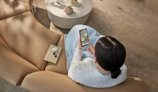 Overhead shot of a woman seated on a curved tan leather sofa using a smartphone, styled by Lauren Knudsen.