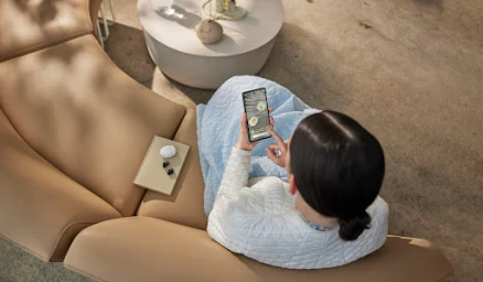 Overhead shot of a woman seated on a curved tan leather sofa using a smartphone, styled by Lauren Knudsen.