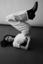 Monochrome image of a model lying on the floor with legs raised wearing white jeans and black boots