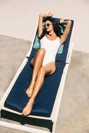 Woman in a white one-piece swimsuit reclining on a blue sun lounger outdoors in Los Angeles.