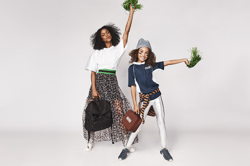 A woman and child, of African descent, cheer with faux grass pompoms in a studio. The child holds a football, posing in sportswear.