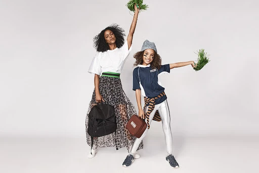 A woman and child, of African descent, cheer with faux grass pompoms in a studio. The child holds a football, posing in sportswear.