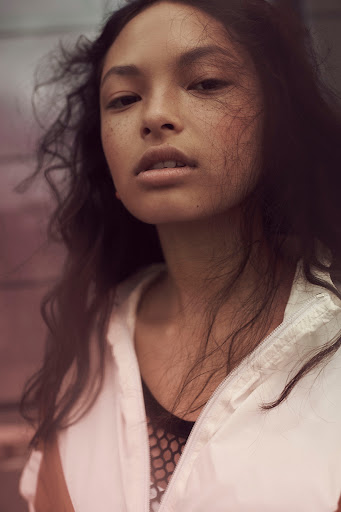 Studio shot of a brunette woman in a black dress posing against a grey backdrop, showcasing hair and makeup artistry.