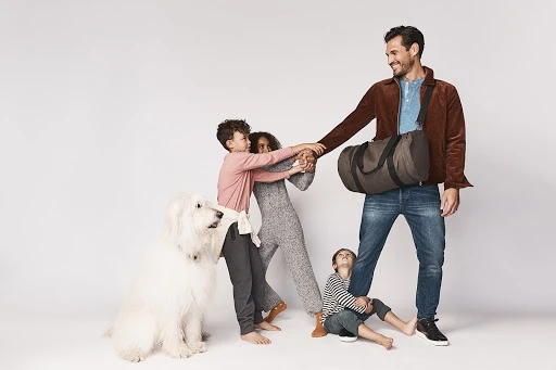 Father in a brown corduroy jacket holding a duffel bag, surrounded by three children and a large white dog