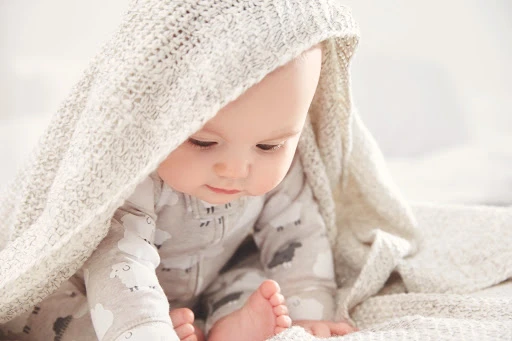 Adorable baby with a cozy knitted blanket. Soft focus, warm lighting. Perfect for baby product advertisements or heartwarming family content.
