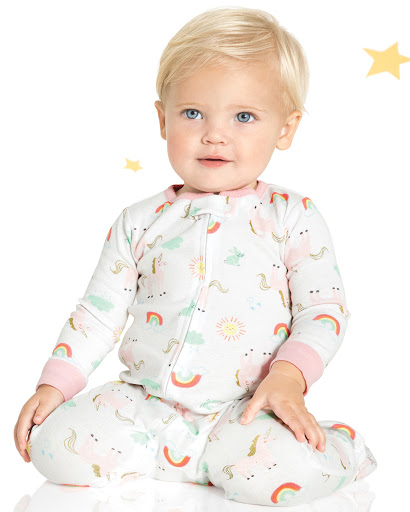 Adorable baby wearing a unicorn-patterned pajama sitting against a white background, illuminated by soft light and whimsical star accents.