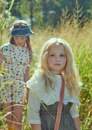 Two young girls in a field of tall grass, one with blond hair wearing a white eyelet top, the other with a blue headband. 