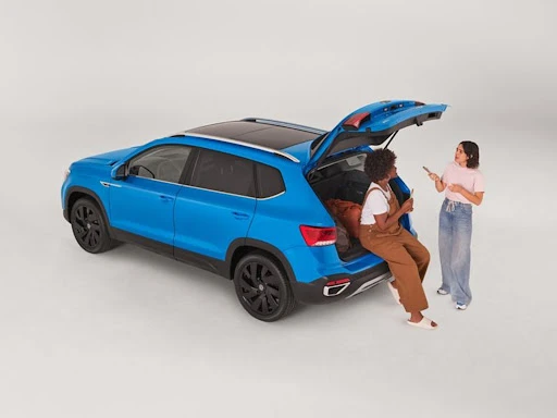 Bright blue SUV with open hatchback on white background, two women with phones stand behind the vehicle.