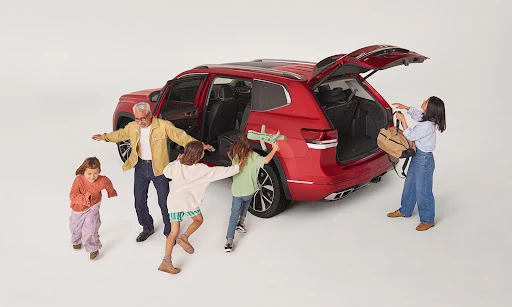 Red SUV with family loading luggage in a white photo studio, including two adult females, one adult male, and three children.
